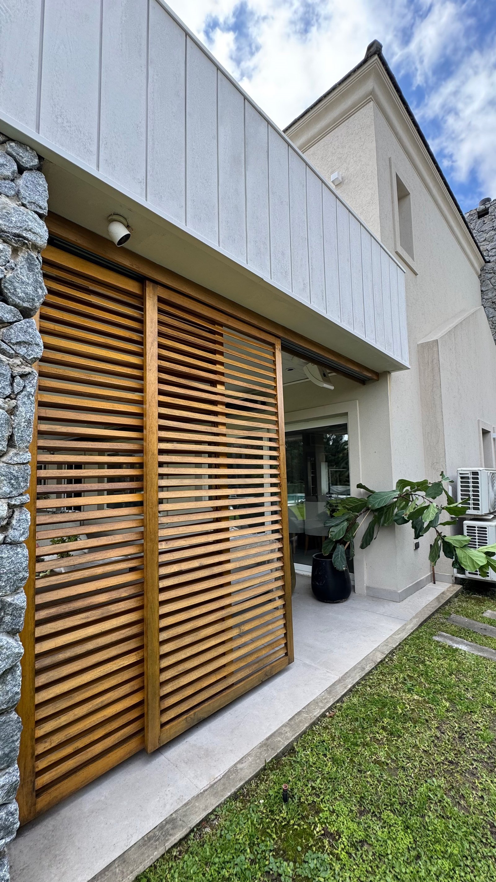 Fachada moderna com portas de correr de madeira e revestimento de pedra — projeto CASA CM, por Hermann Arquitectos, em Los Castores